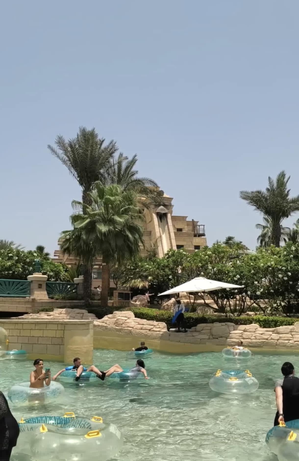 Families floating along the Lazy River at Aquaventure Waterpark Dubai, surrounded by tropical greenery and clear skies.