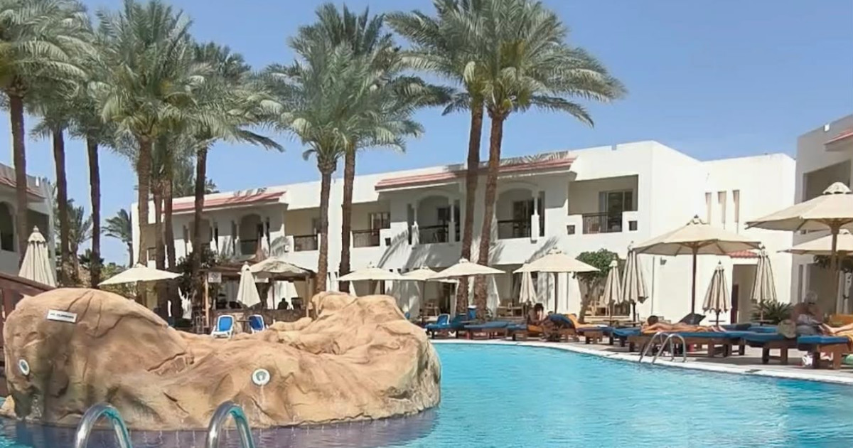 The outdoor swimming pool area at Experience St. George Homestay in Sharm El Sheikh, featuring sun loungers, palm trees, and resort buildings.